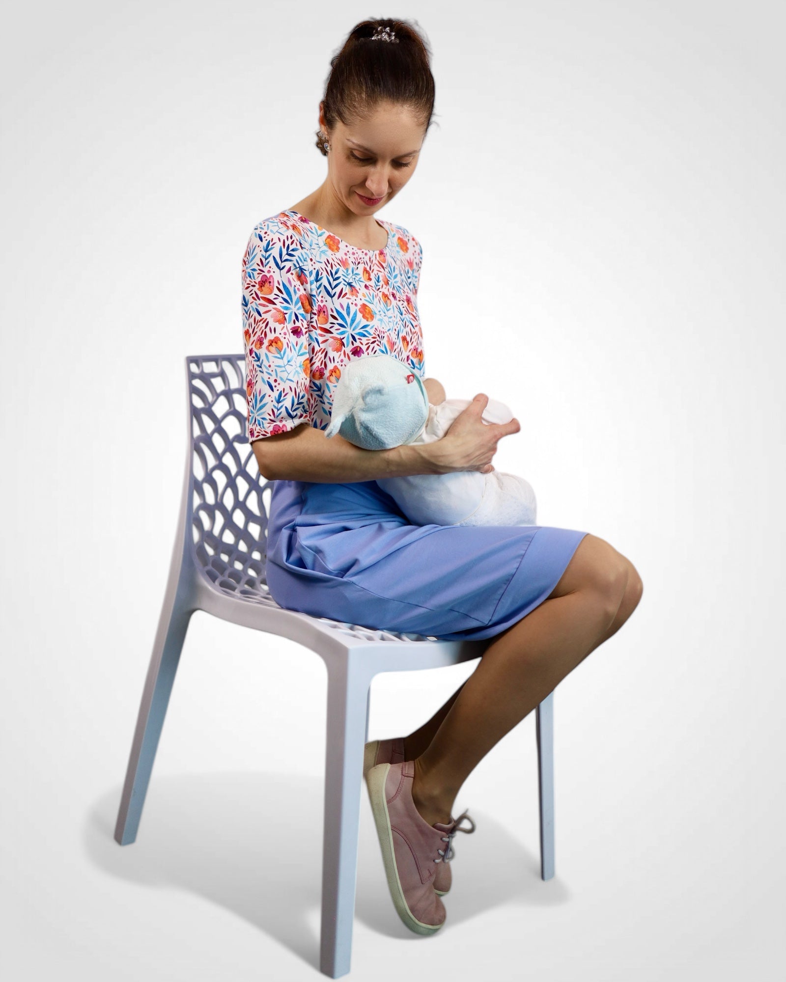 Mama dojčí bábätko v letných kojo šatách s kvetinovým vrchom a svetlomodrou sukňou.