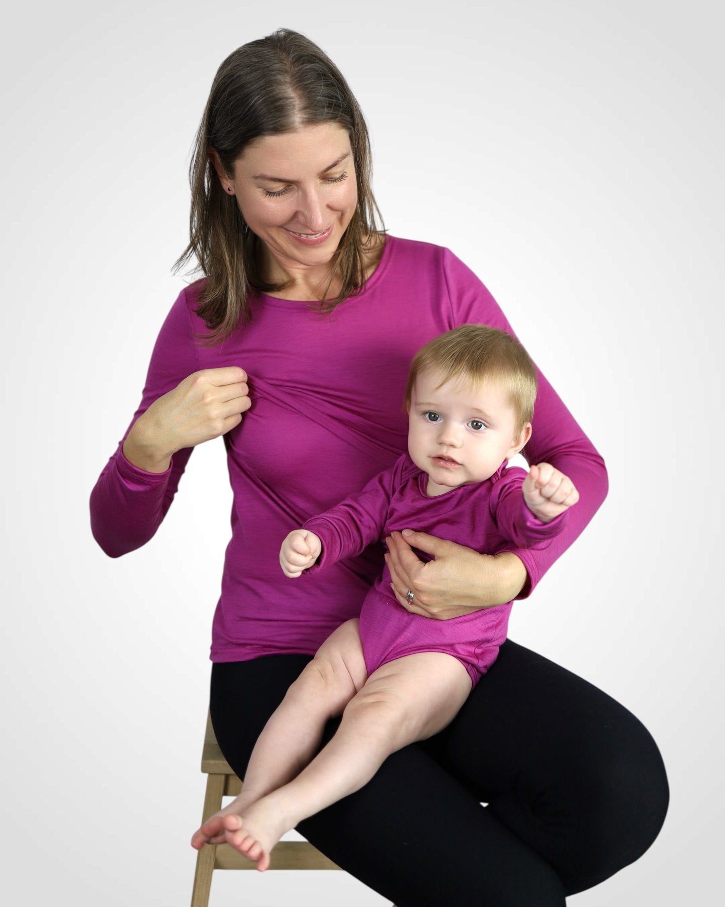 Mama v cyklaménovom merino kojo tričku drží bábätko v rastúcom body z rovnakého materiálu a farby.